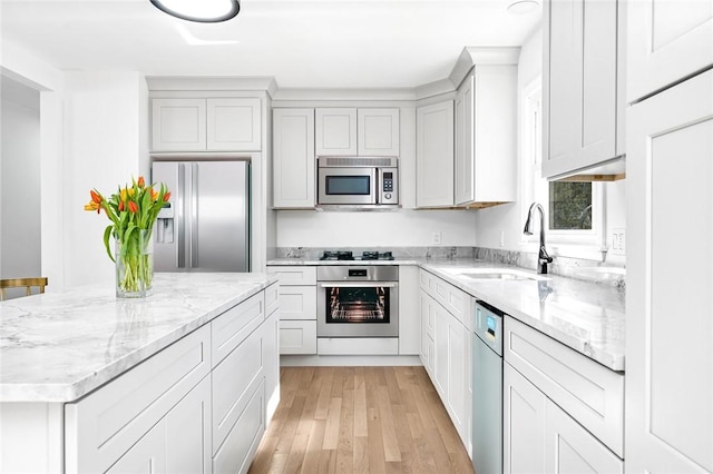 kitchen featuring light stone counters, a sink, light wood-type flooring, appliances with stainless steel finishes, and a kitchen island