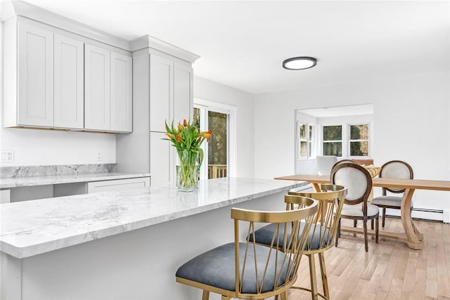 kitchen with a baseboard heating unit, light wood finished floors, light stone countertops, and a breakfast bar