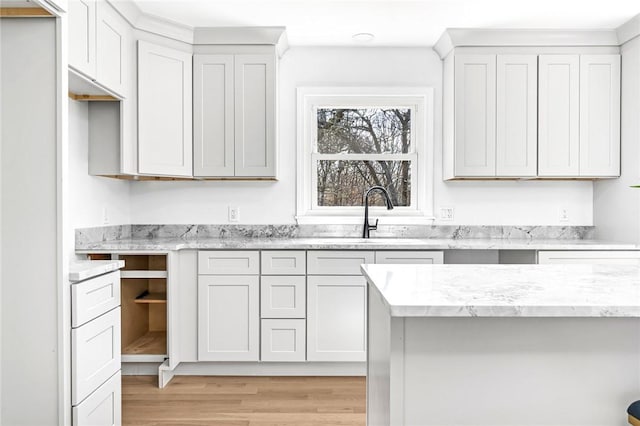 kitchen with light wood-style flooring, light stone counters, and a sink
