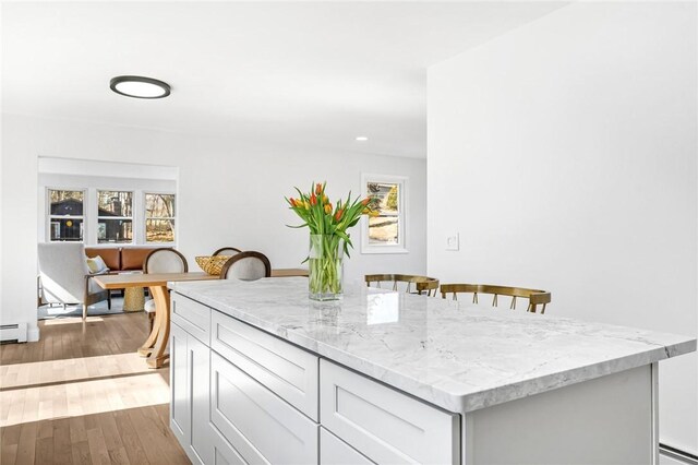 kitchen with baseboard heating, light stone counters, a kitchen breakfast bar, wood finished floors, and a kitchen island