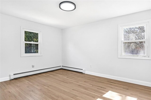unfurnished room featuring a baseboard heating unit, a healthy amount of sunlight, and light wood-style flooring