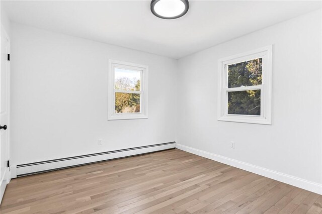 spare room with a baseboard radiator, baseboards, and light wood-style floors