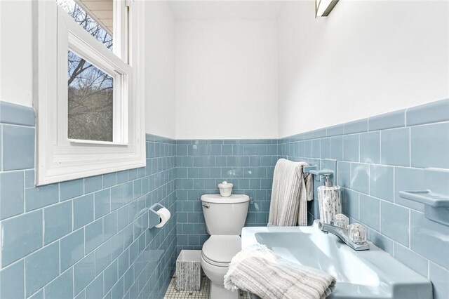 half bathroom featuring tile walls, wainscoting, a sink, and toilet