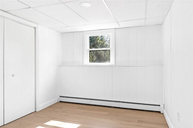 unfurnished room featuring a baseboard radiator, wood finished floors, and a drop ceiling
