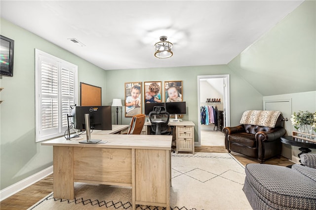 home office featuring baseboards, vaulted ceiling, light wood-style flooring, and visible vents