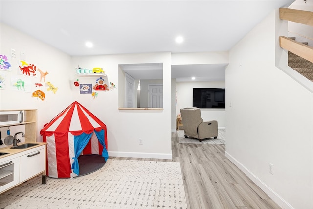recreation room with a sink, baseboards, recessed lighting, and light wood-style flooring