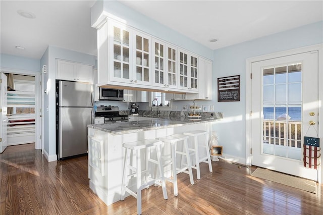 57 Foster St, Warwick, RI 02889 - kitchen with a peninsula, stainless steel appliances, white cabinetry, glass insert cabinets, and light stone countertops