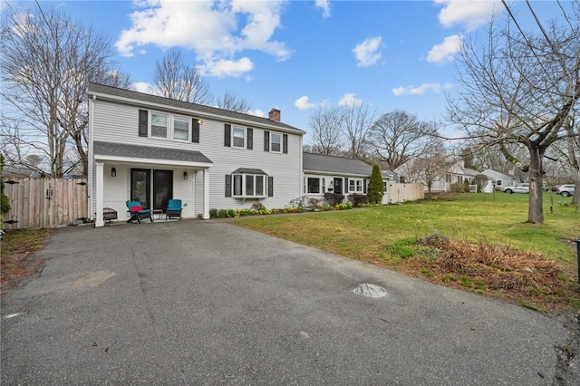 view of front of home with a front yard, driveway, fence, and a chimney