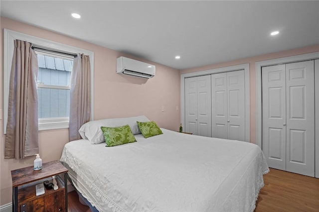 bedroom with recessed lighting, two closets, a wall unit AC, and wood finished floors