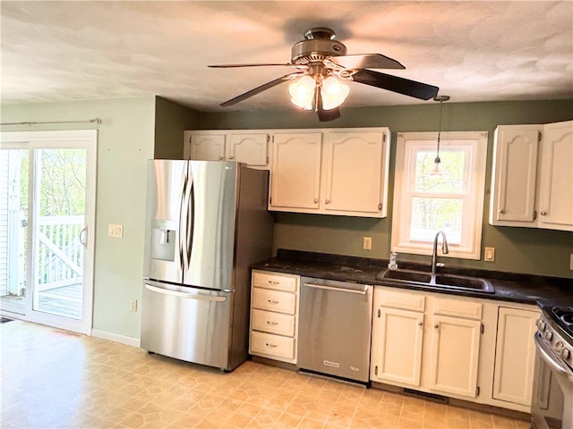 kitchen featuring appliances with stainless steel finishes, a sink, dark countertops, a ceiling fan, and hanging light fixtures