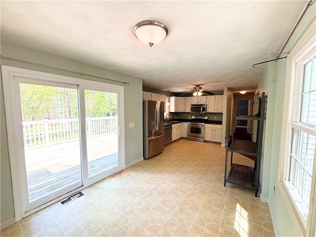kitchen featuring appliances with stainless steel finishes, dark countertops, a sink, baseboards, and a ceiling fan