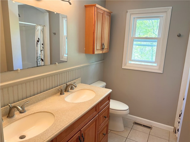 bathroom with tile patterned flooring, toilet, a shower with shower curtain, double vanity, and a wainscoted wall
