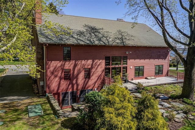 rear view of property with a patio area, roof with shingles, and a chimney