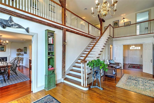 stairway featuring wood finished floors, a decorative wall, a high ceiling, a wainscoted wall, and a chandelier