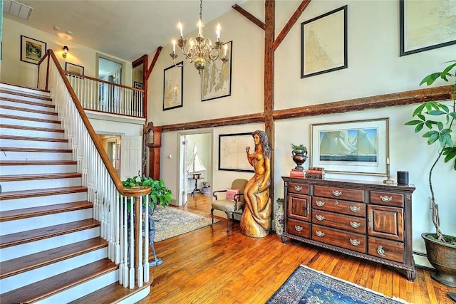 stairs with visible vents, baseboard heating, an inviting chandelier, a high ceiling, and hardwood / wood-style floors