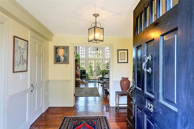 entrance foyer featuring a chandelier, dark wood-style floors, ornamental molding, and a wainscoted wall