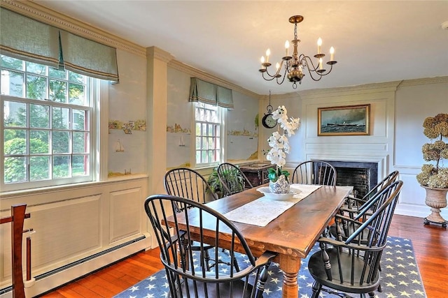 dining space featuring crown molding, a notable chandelier, a fireplace, wood finished floors, and a baseboard radiator