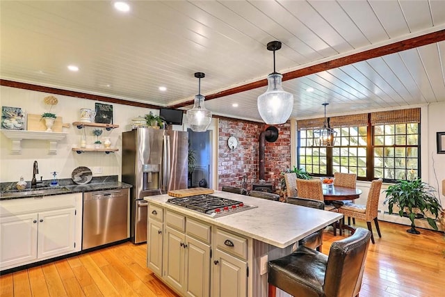kitchen with a sink, a wood stove, light wood-style floors, a center island, and stainless steel appliances