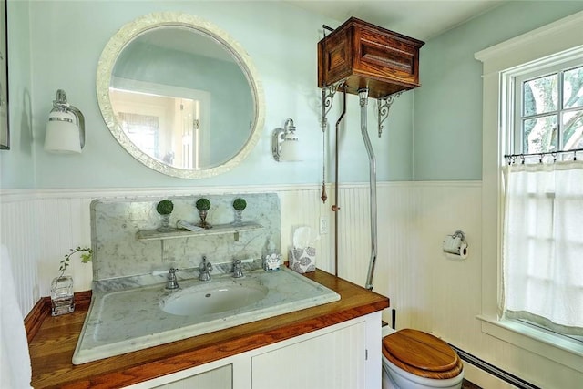 bathroom featuring vanity, toilet, baseboard heating, and a wainscoted wall