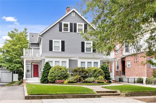 traditional style home featuring fence, a chimney, a balcony, and a front lawn