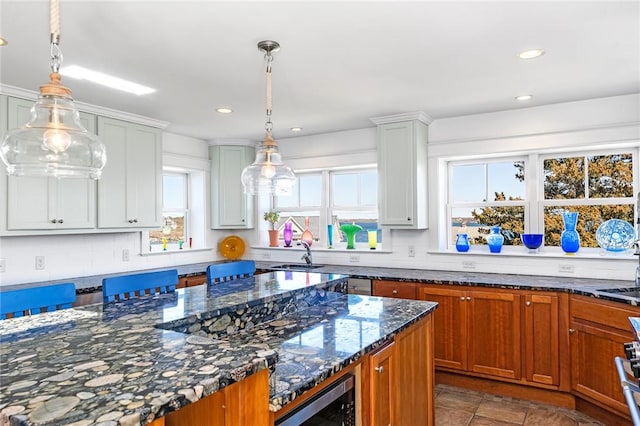 kitchen with dark stone countertops, stainless steel microwave, a sink, recessed lighting, and hanging light fixtures