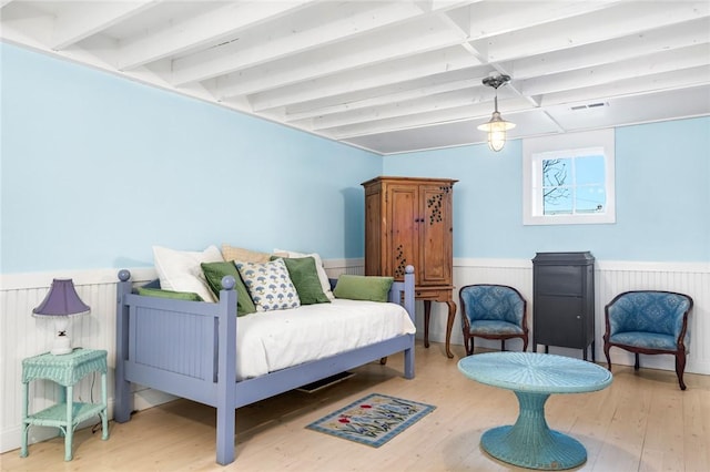 bedroom featuring beam ceiling, wood finished floors, visible vents, and a wainscoted wall