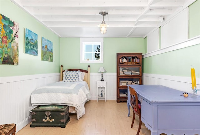 bedroom featuring beam ceiling, a wainscoted wall, and light wood-style flooring