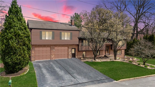split level home with driveway, a chimney, a front yard, brick siding, and a garage