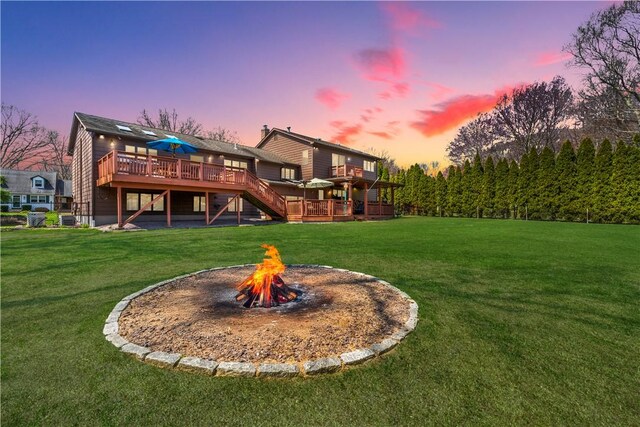 rear view of property featuring a lawn, a wooden deck, stairway, and a fire pit