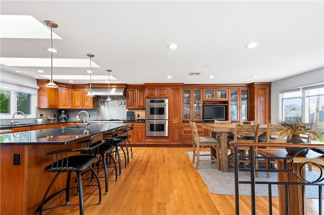kitchen featuring double oven, a breakfast bar, brown cabinets, and light wood-type flooring