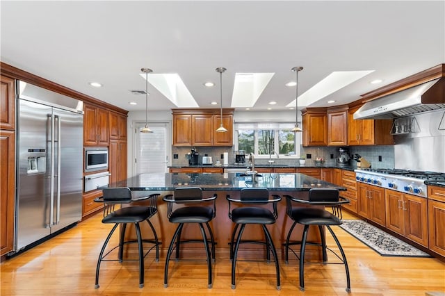kitchen featuring a skylight, light wood-style flooring, decorative backsplash, a warming drawer, and built in appliances