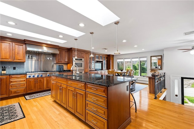 kitchen featuring a skylight, light wood-style flooring, a kitchen bar, visible vents, and wall chimney exhaust hood