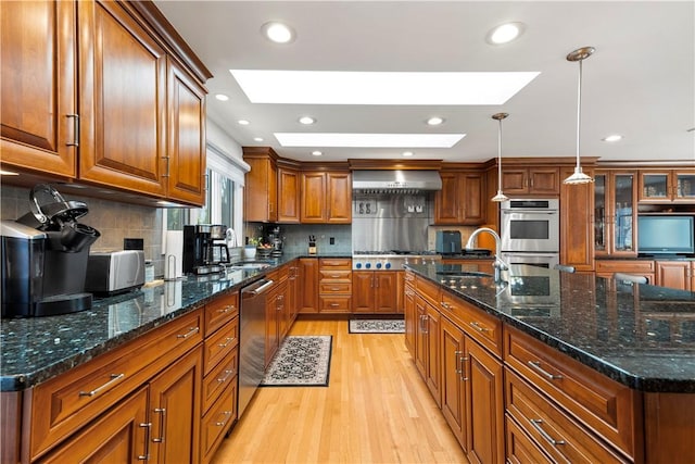 kitchen with brown cabinets, a sink, appliances with stainless steel finishes, light wood finished floors, and a skylight