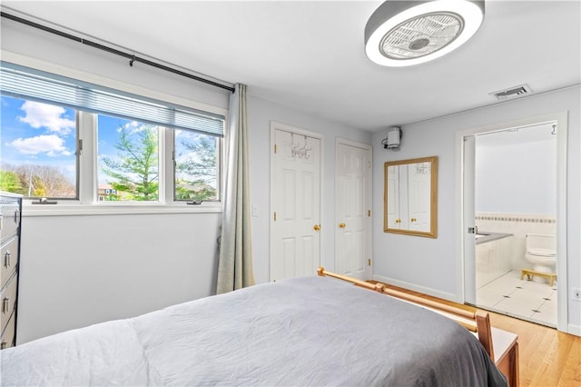 bedroom featuring wood finished floors, connected bathroom, and visible vents