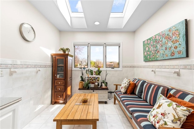 living area featuring light tile patterned flooring, tile walls, a skylight, and wainscoting