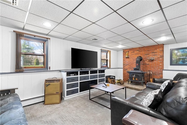 living room featuring a wood stove, a paneled ceiling, visible vents, carpet, and baseboard heating
