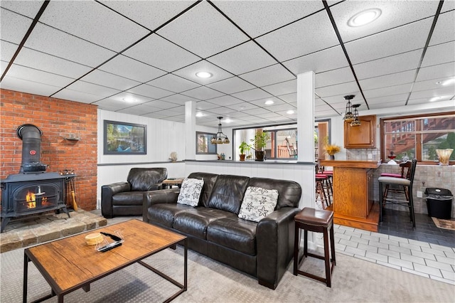 living area with a wood stove, light tile patterned floors, indoor bar, and a drop ceiling