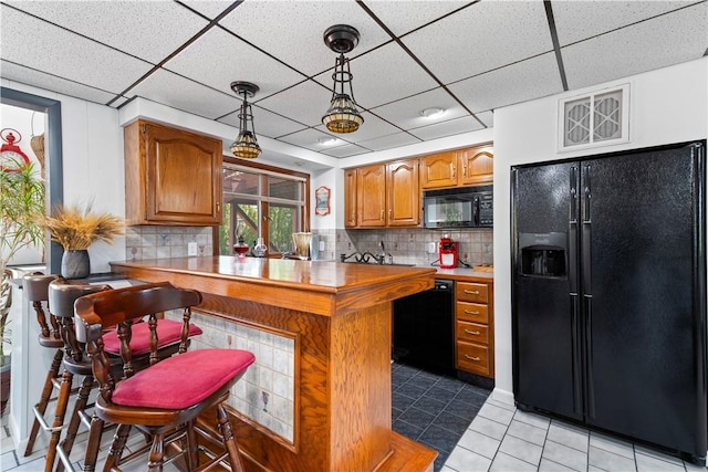 kitchen with light tile patterned floors, black appliances, brown cabinets, and backsplash