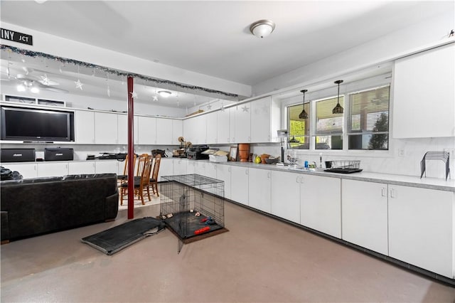 kitchen featuring a sink, concrete flooring, white cabinetry, light countertops, and hanging light fixtures