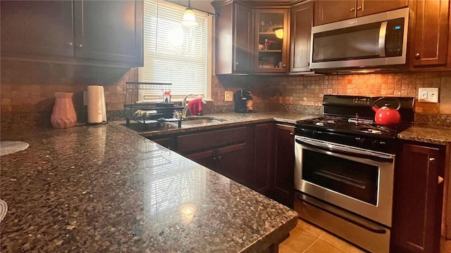 kitchen with glass insert cabinets, dark stone countertops, backsplash, hanging light fixtures, and appliances with stainless steel finishes