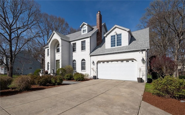 view of front of house featuring a chimney, brick siding, concrete driveway, and roof with shingles