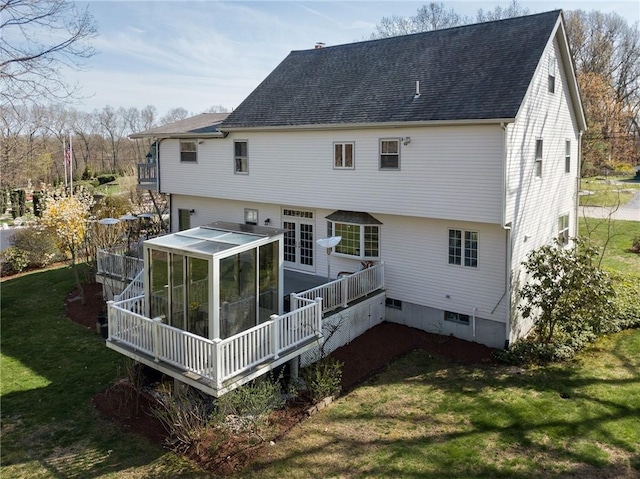 rear view of house with a lawn, a shingled roof, and a sunroom