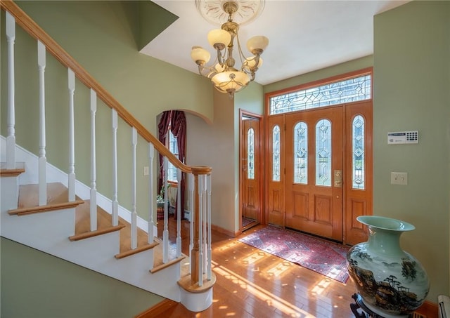 foyer entrance featuring hardwood / wood-style floors, a notable chandelier, a baseboard heating unit, and stairs