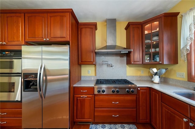 kitchen with wall chimney range hood, glass insert cabinets, a sink, stainless steel appliances, and light countertops