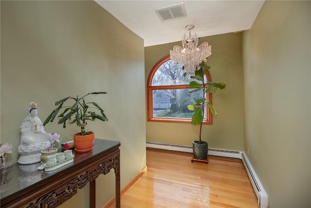 interior space featuring a baseboard radiator, visible vents, baseboards, an inviting chandelier, and wood finished floors