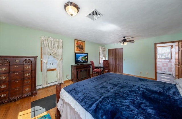 bedroom with a baseboard radiator, visible vents, baseboard heating, baseboards, and wood finished floors