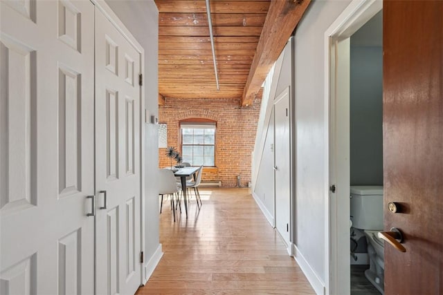 corridor featuring baseboards, light wood finished floors, brick wall, and wood ceiling