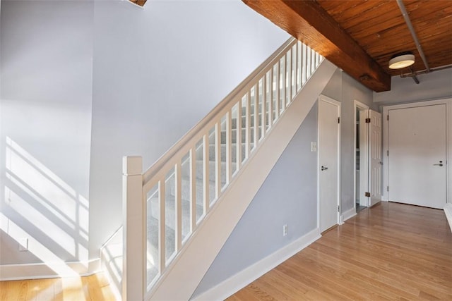 stairs with beam ceiling, wooden ceiling, wood finished floors, and baseboards