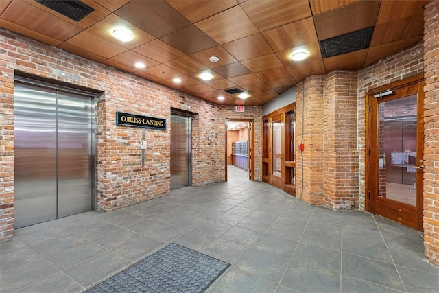 hall with elevator, visible vents, and brick wall