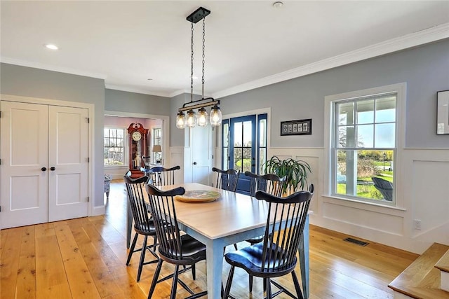 dining area featuring visible vents, light wood finished floors, a decorative wall, and wainscoting